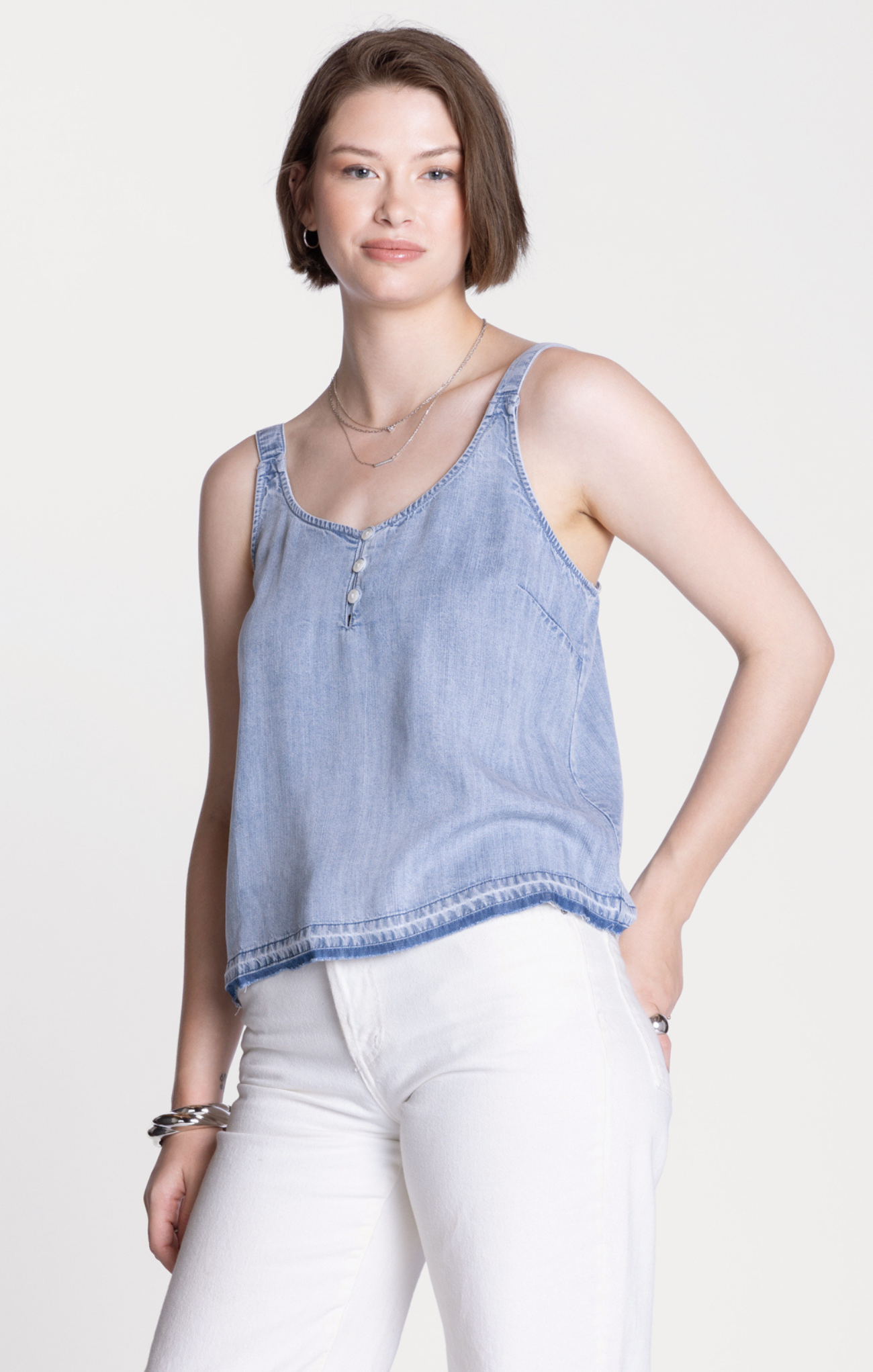 Woman wearing a light blue denim tank top and white pants on a white background