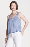 Woman wearing a light blue denim tank top and white pants on a white background