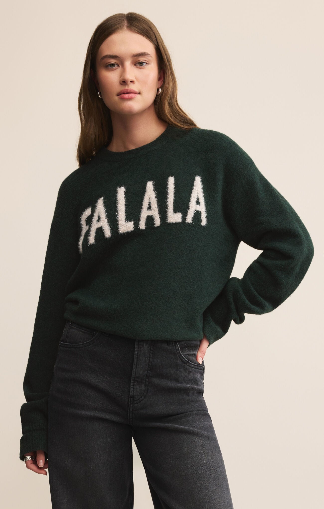 Person wearing a dark green sweater with 'FA LA LA' text on a beige background