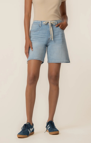Person wearing light blue denim shorts on a beige background