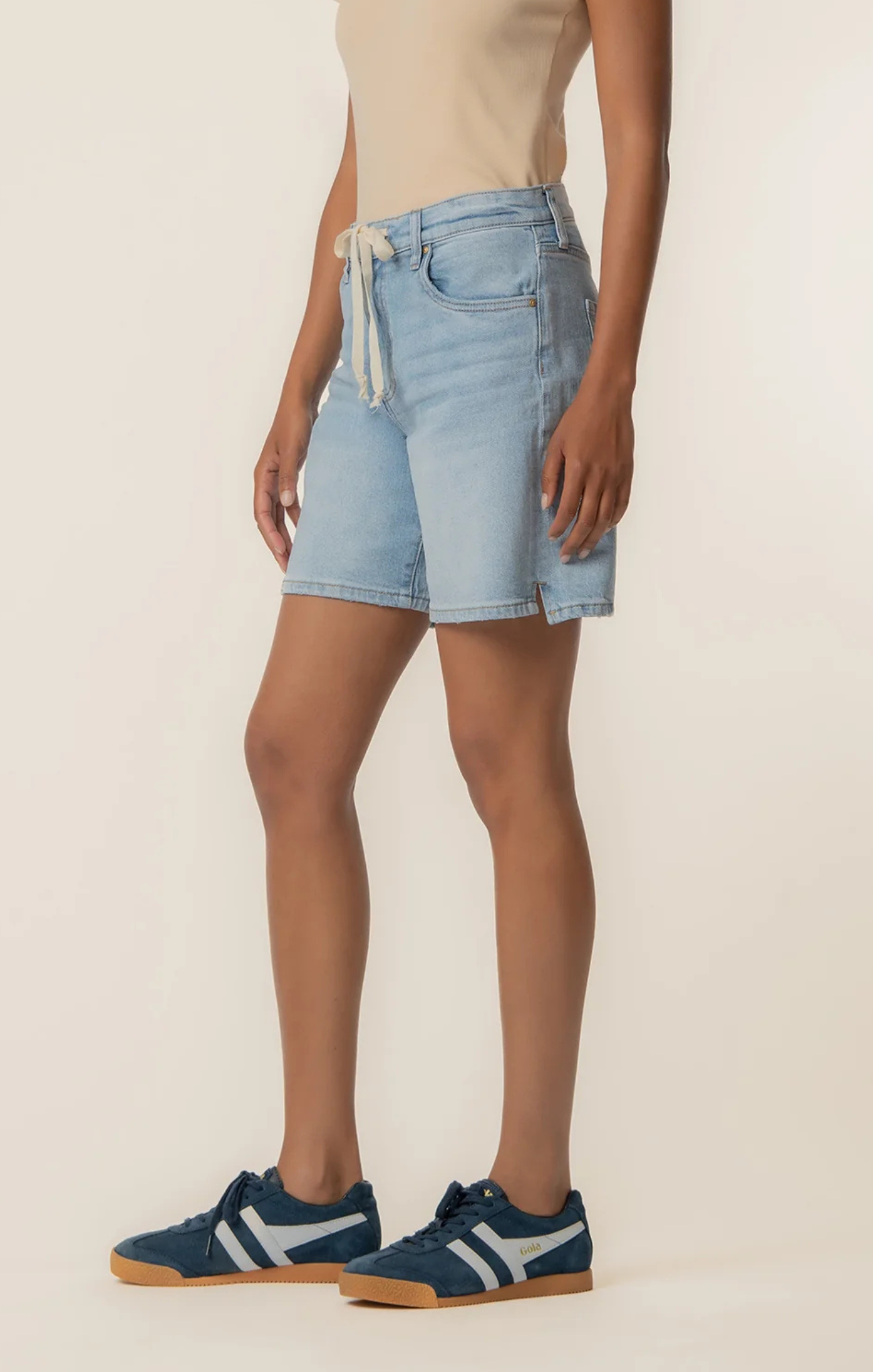 Person wearing light blue denim shorts on a beige background