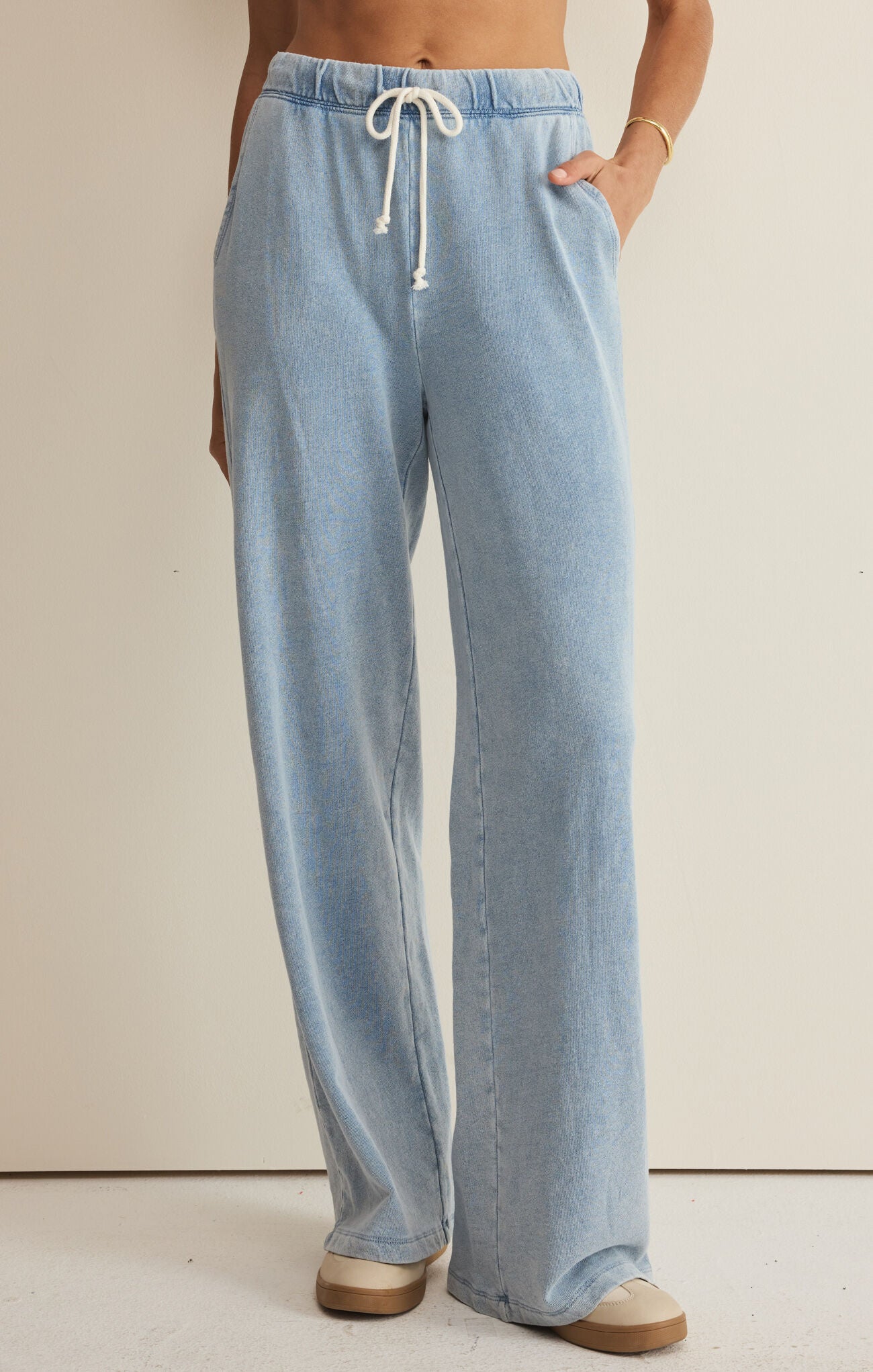 Light blue denim pants with a drawstring on a beige background