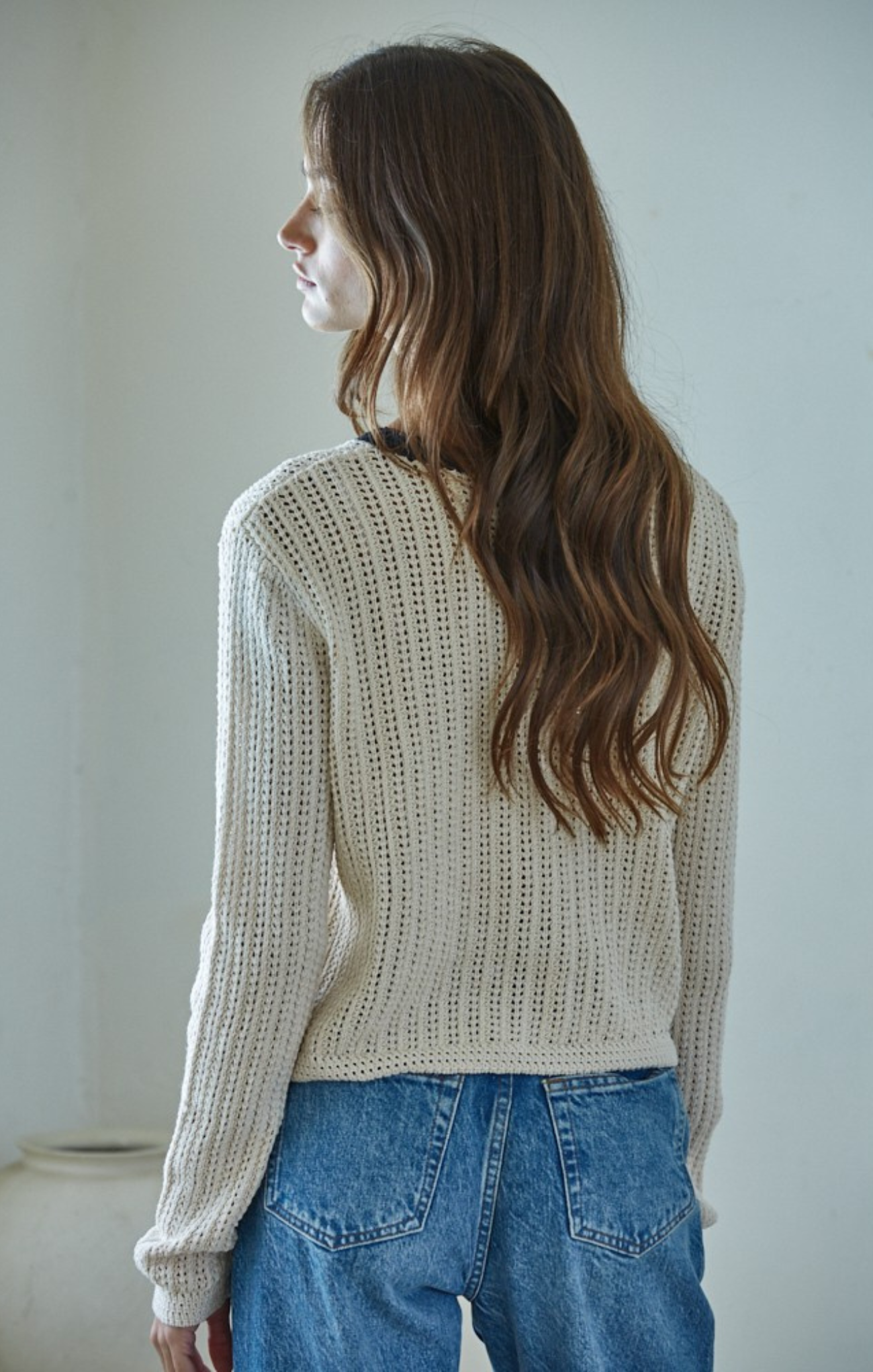 Woman wearing a beige knitted sweater and blue jeans against a plain background