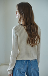 Woman wearing a beige knitted sweater and blue jeans against a plain background