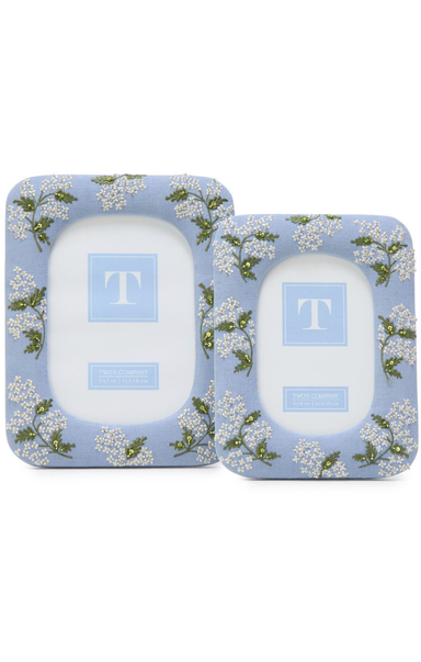 Two white candles with 'T' branding on blue floral packaging.