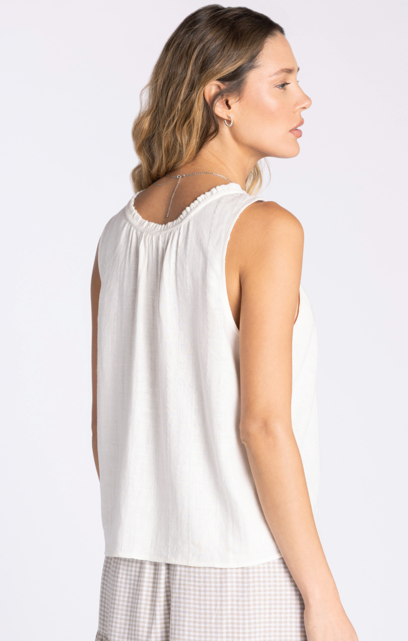 Woman wearing a white sleeveless top on a plain background