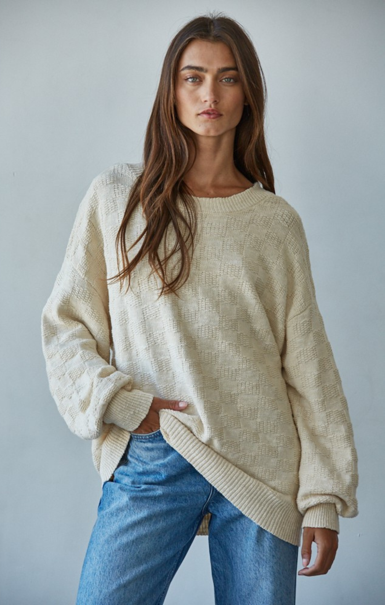 Woman in cream sweater with blue jeans with hand in pocket