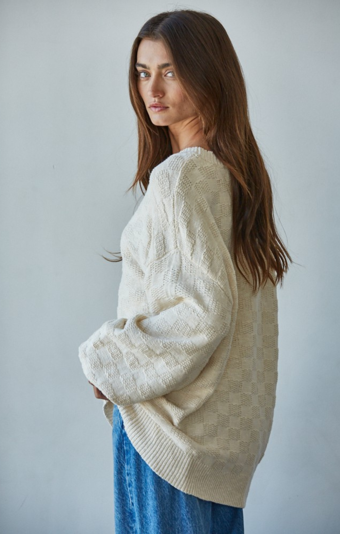 Woman in cream sweater with blue jeans with hand in pocket
