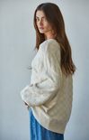 Woman in cream sweater with blue jeans with hand in pocket