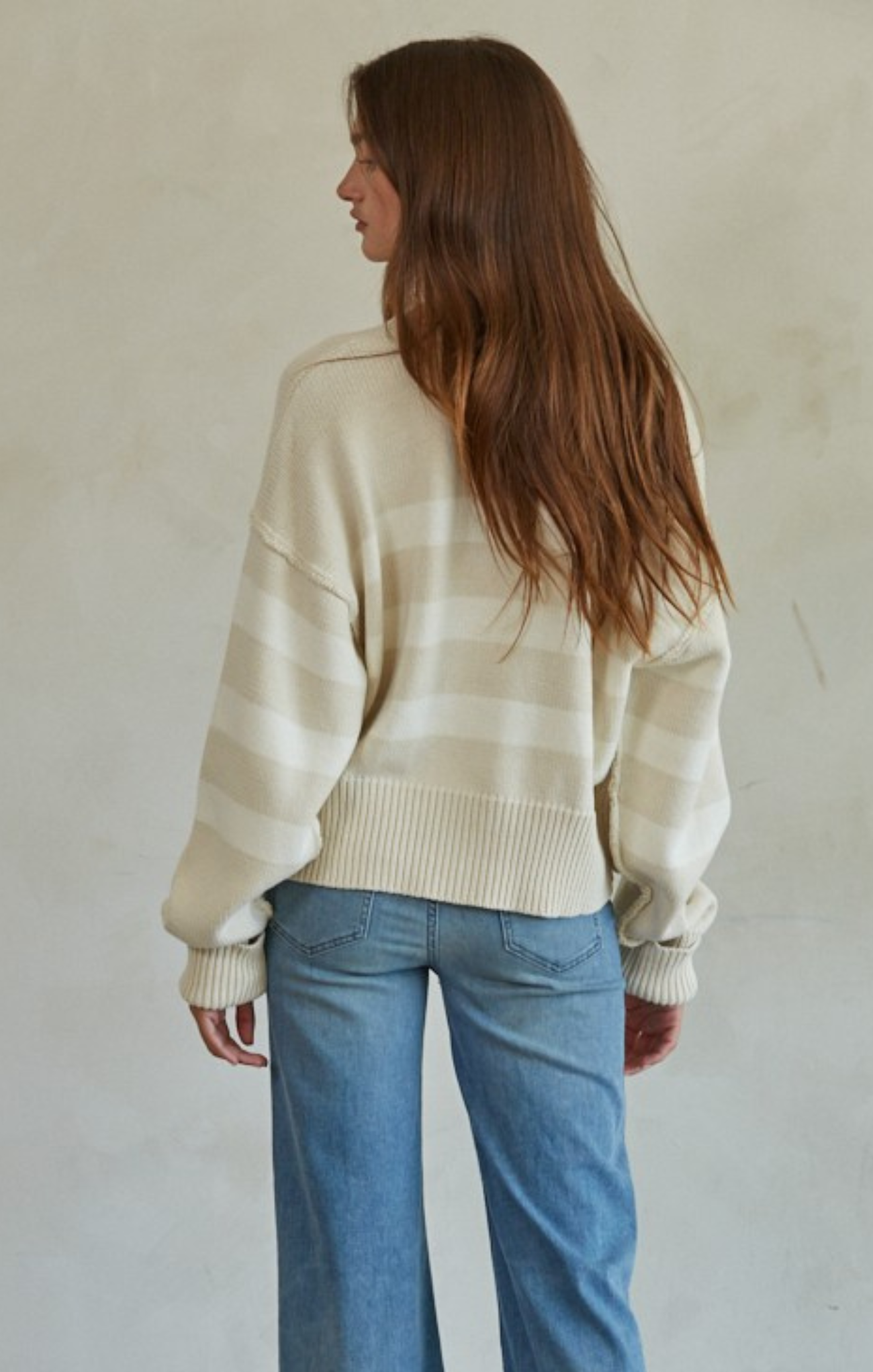 Woman wearing a striped sweater and blue jeans against a plain background