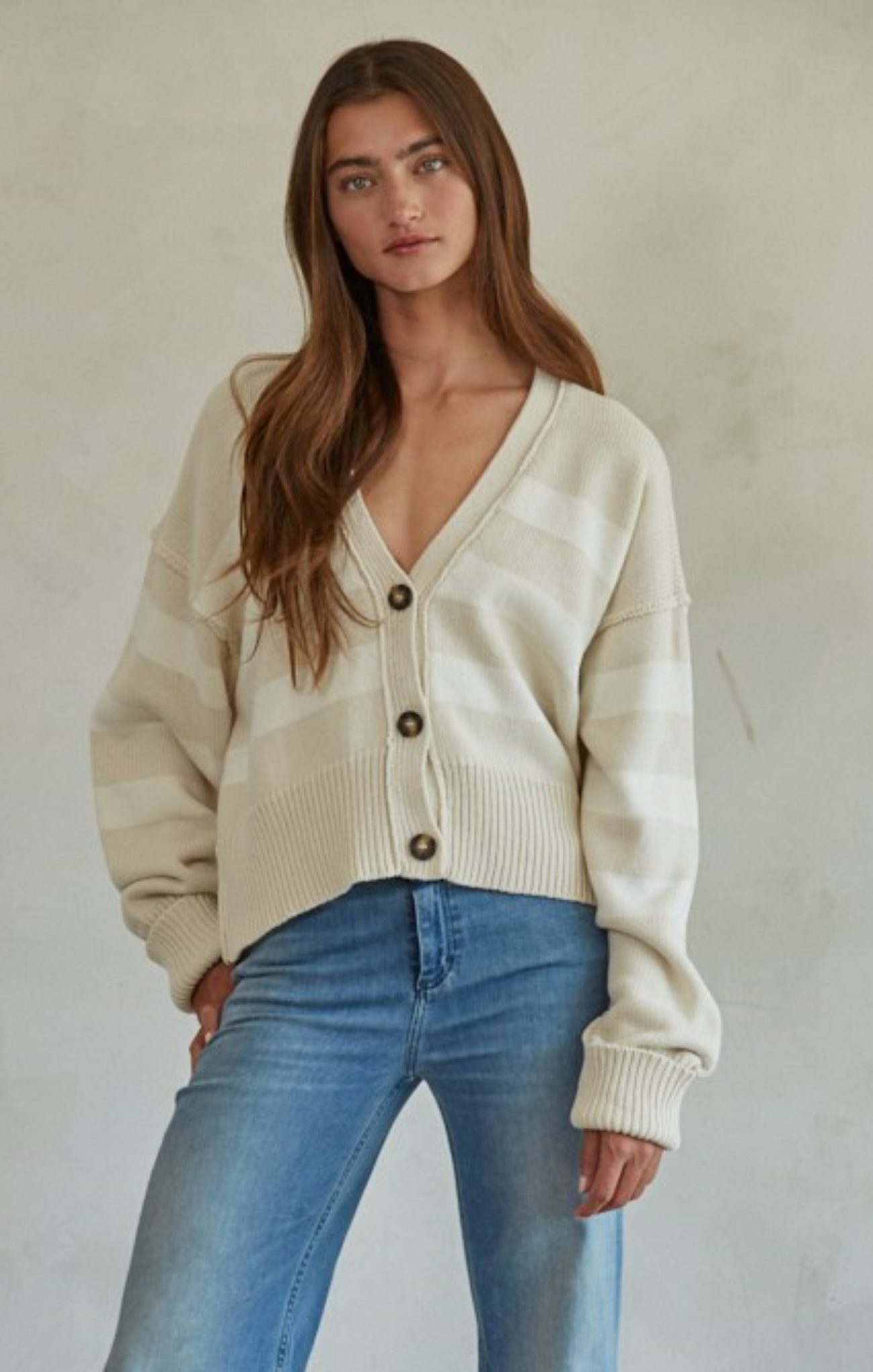Woman wearing a cream cardigan and blue jeans against a plain background