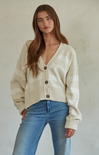 Woman wearing a cream cardigan and blue jeans against a plain background