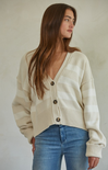 Woman wearing a cream cardigan and blue jeans against a plain background