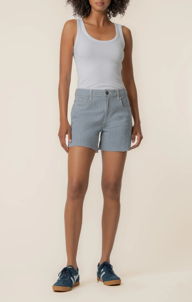 Woman wearing a white tank top and blue checkered shorts on a beige background
