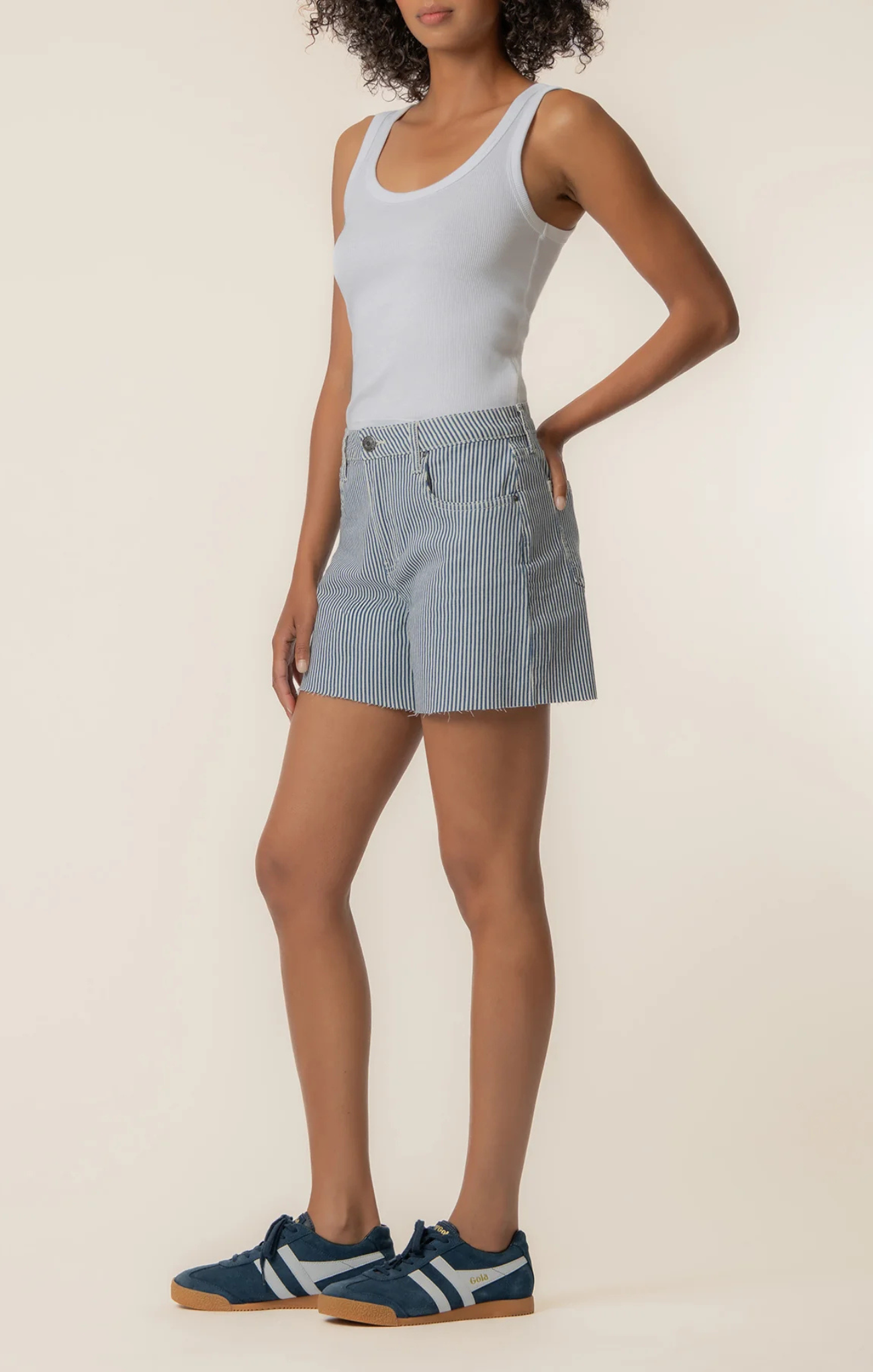 Woman wearing a light blue tank top and striped shorts on a beige background