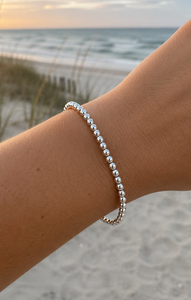 Silver beaded bracelet on a wrist with a beach background