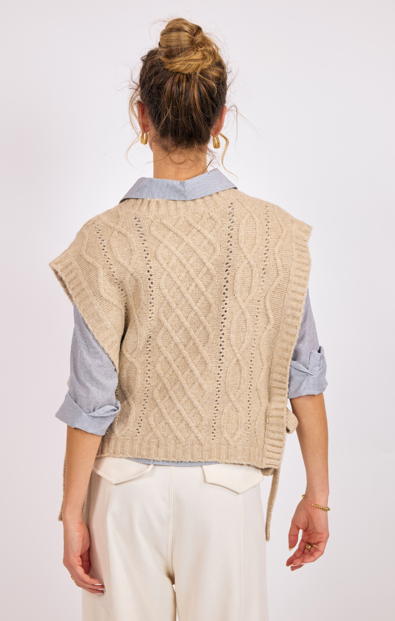 Person wearing a beige knitted vest over a blue shirt on a white background