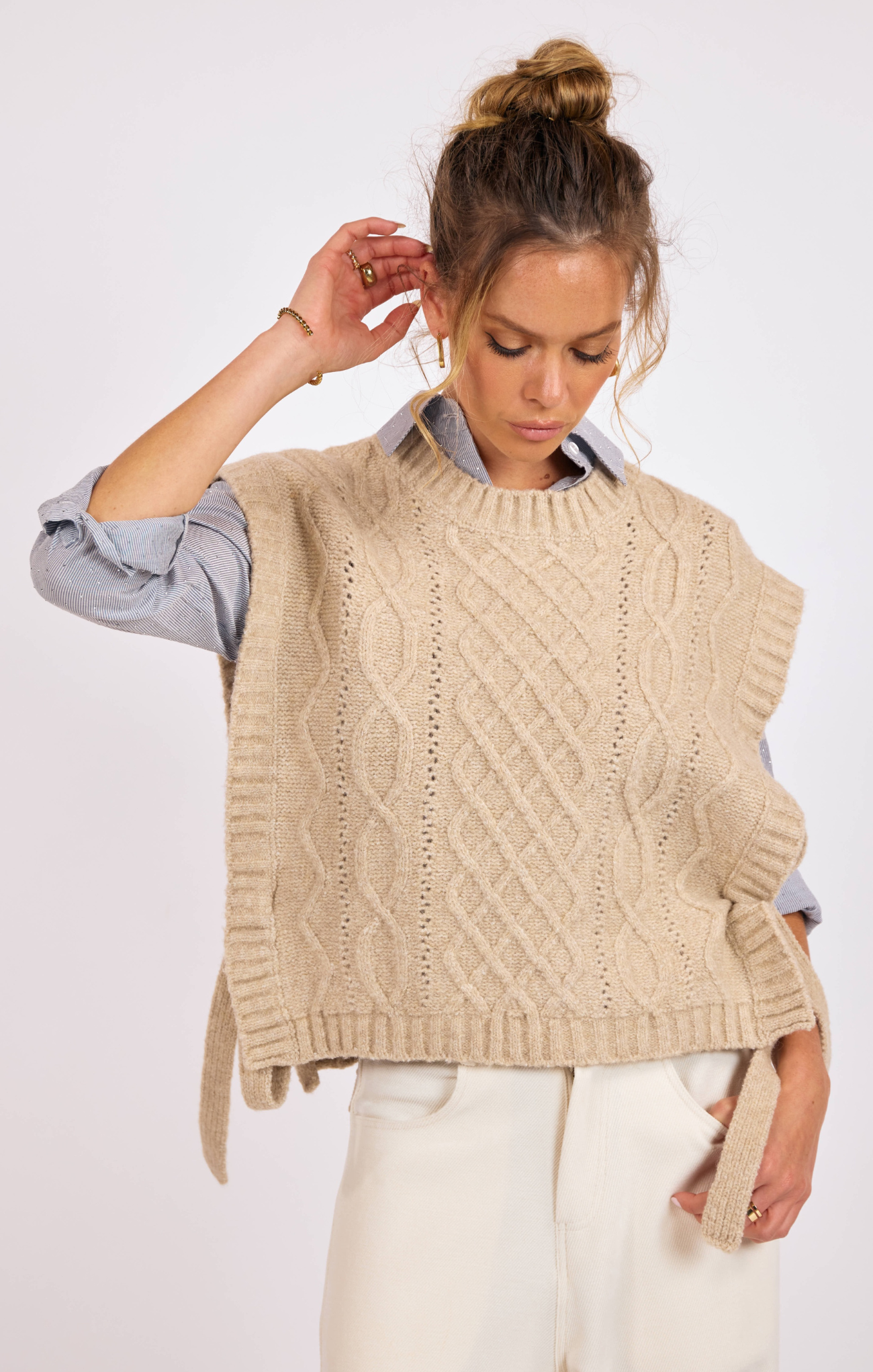 Woman wearing a beige knitted vest over a light blue shirt on a white background
