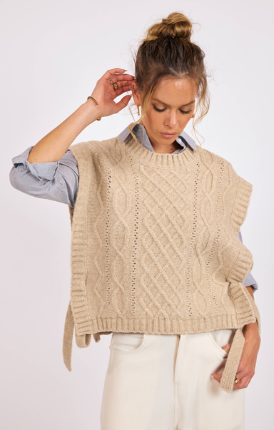 Woman wearing a beige knitted vest over a light blue shirt on a white background