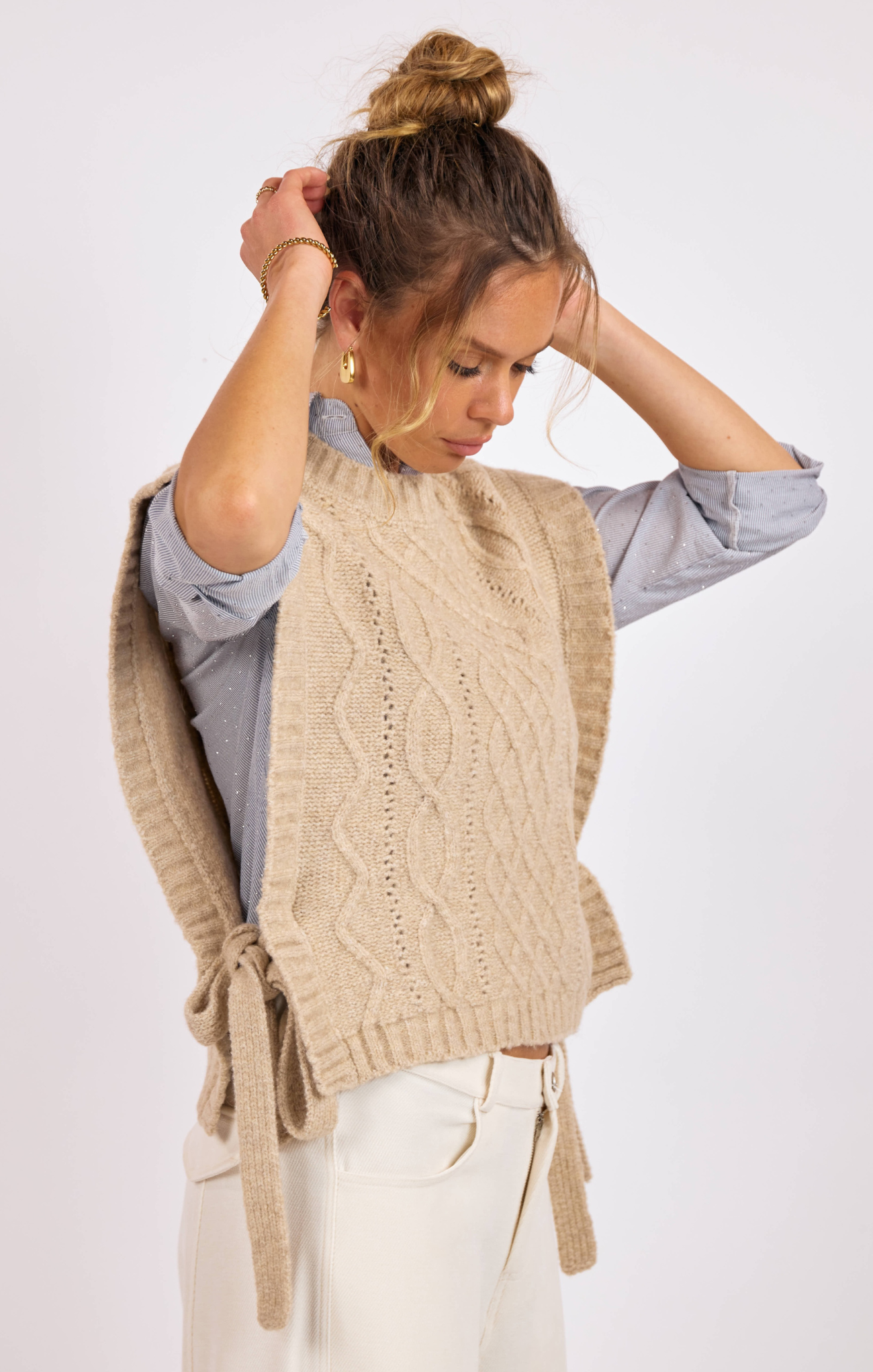 Woman wearing a beige knitted vest over a light blue shirt on a white background