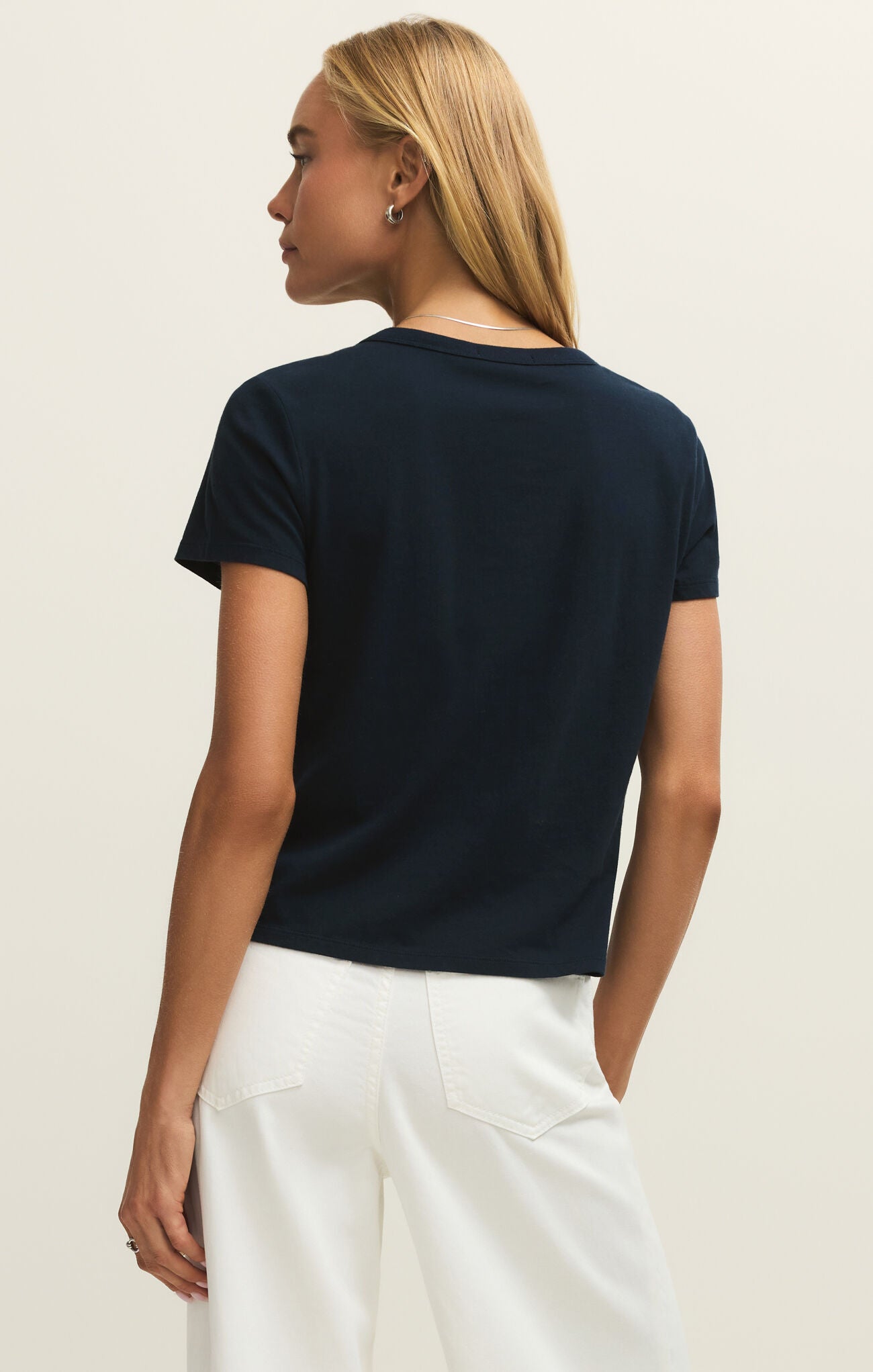 Woman wearing a navy blue t-shirt and white pants on a beige background