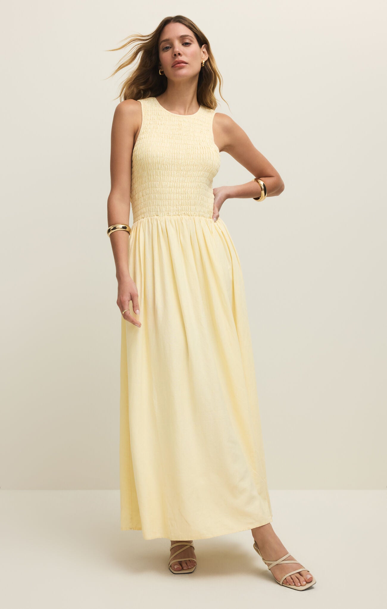 Woman wearing a light yellow sleeveless dress against a white background