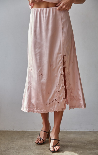 Pink skirt with floral embroidery worn by a person on a plain background
