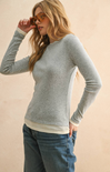 Woman wearing a gray sweater and blue jeans against a beige background