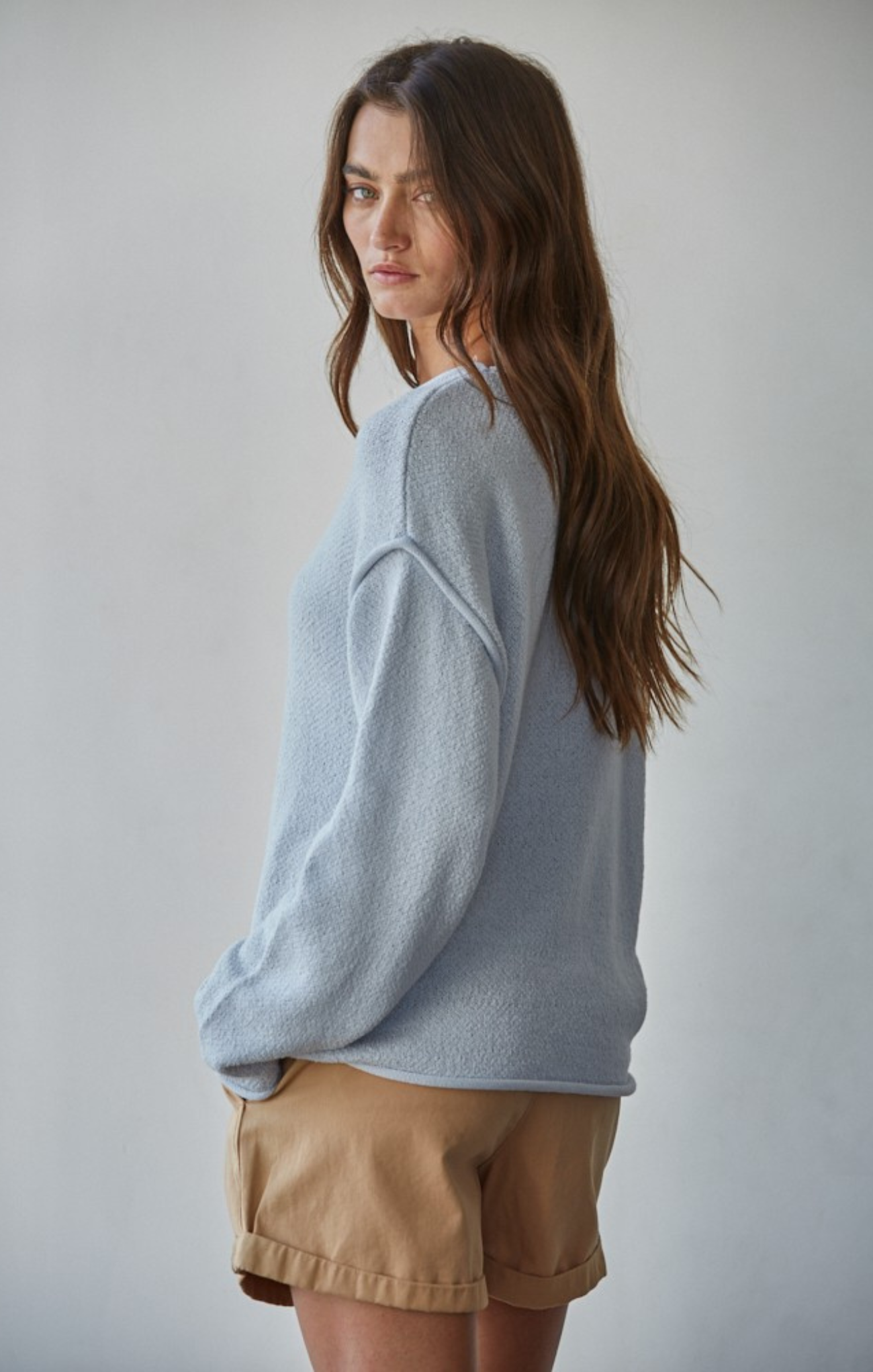 Woman wearing a light blue sweater and beige shorts against a plain background