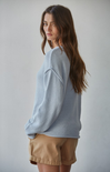Woman wearing a light blue sweater and beige shorts against a plain background