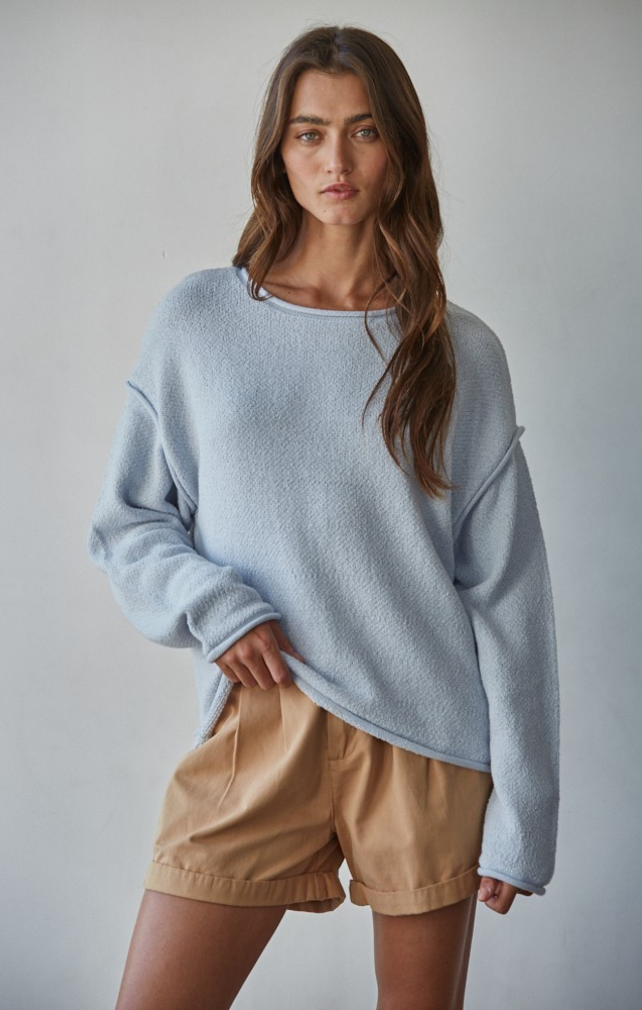Woman wearing a light blue sweater and beige shorts against a plain background