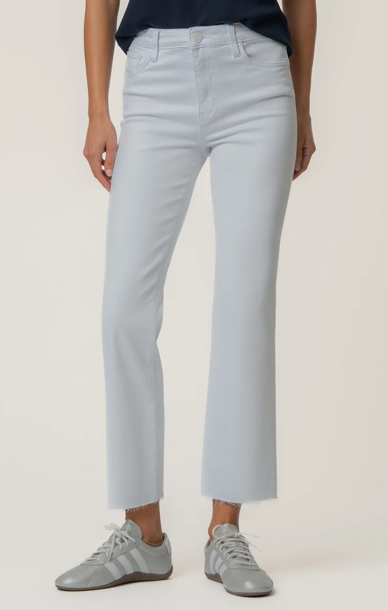 Person wearing light gray jeans and gray sneakers on a plain background