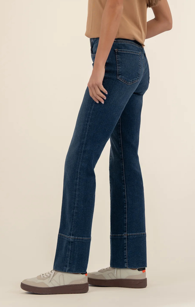 Person wearing dark-wash high-rise flare jeans with front seam detailing, paired with a tan top and light gray sneakers, shown from shoulders to feet against a neutral background.