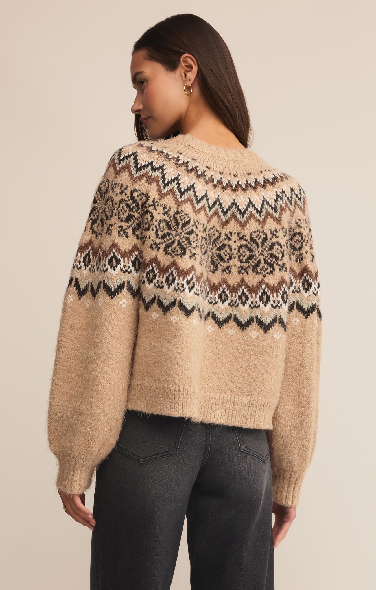 Woman wearing a beige sweater with a patterned design on a plain background