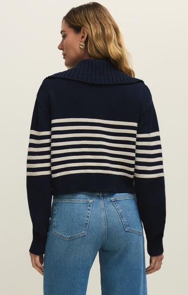 Person wearing a navy and white striped sweater with blue jeans on a beige background