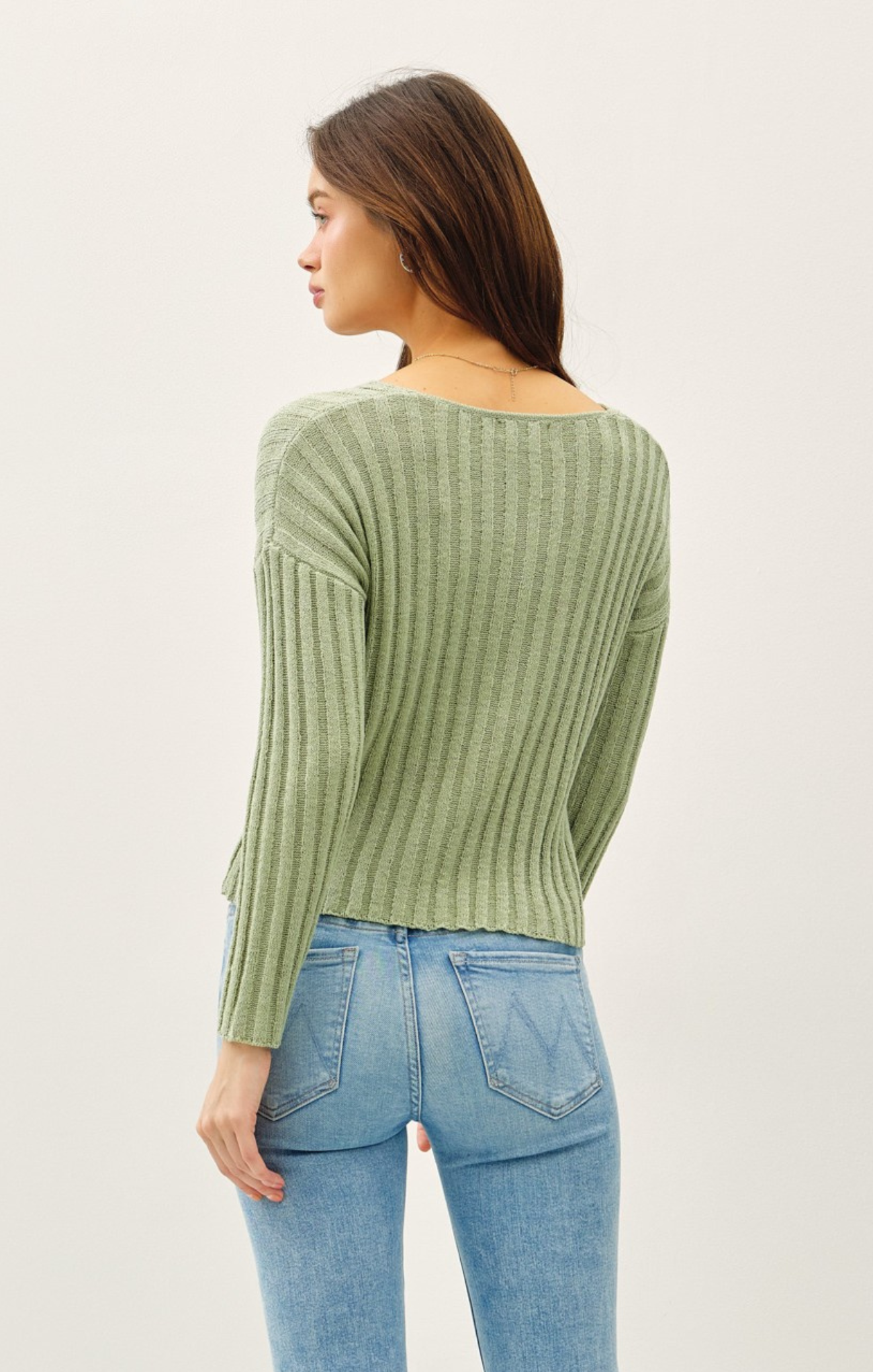 Woman wearing a green ribbed sweater and blue jeans on a white background