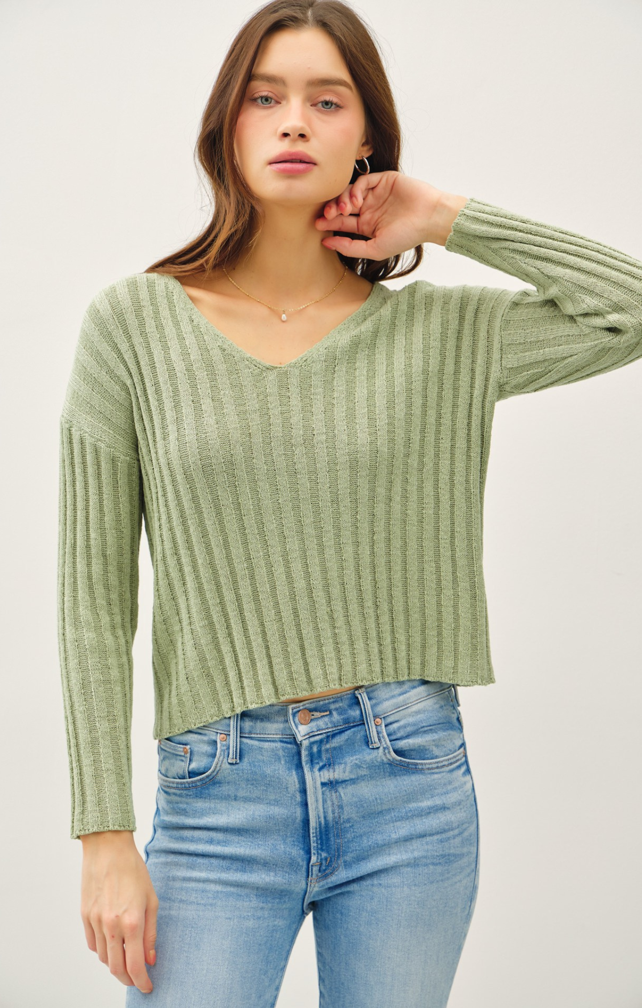 Woman wearing a green ribbed sweater and blue jeans on a white background