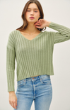 Woman wearing a green ribbed sweater and blue jeans on a white background