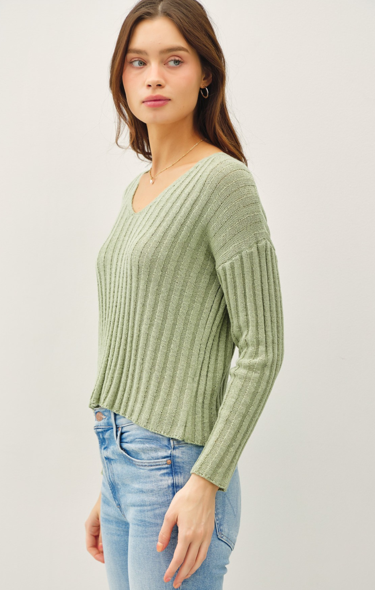 Woman wearing a green ribbed sweater and blue jeans on a light gray background