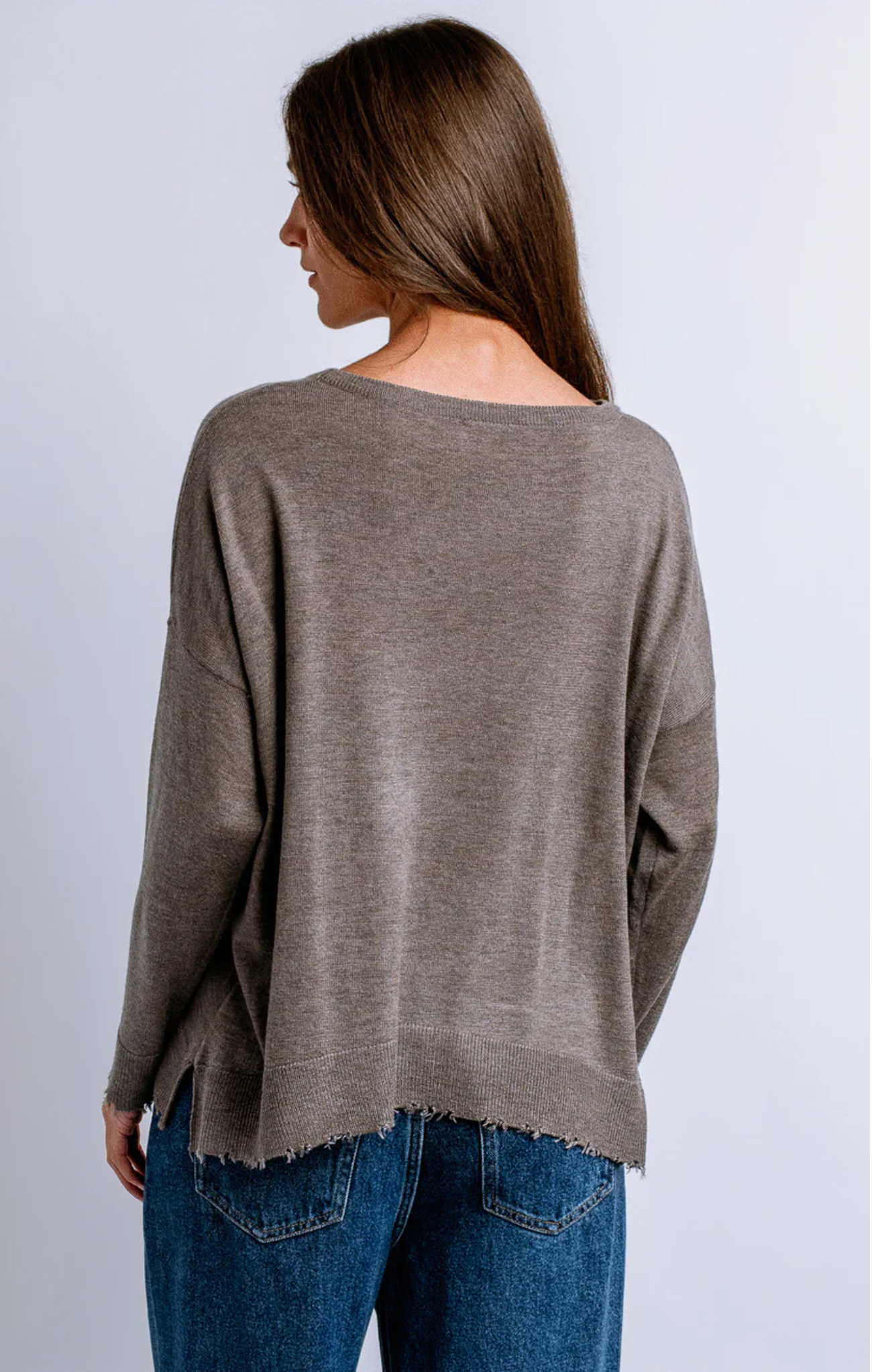 Woman wearing a brown sweater and blue jeans on a white background