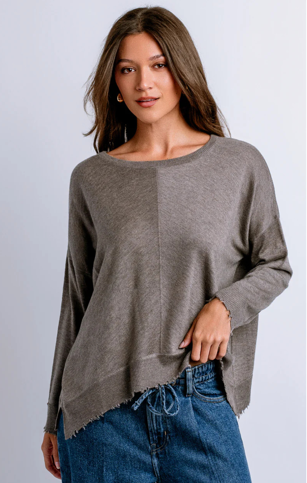 Woman wearing a gray sweater and blue jeans against a light gray background