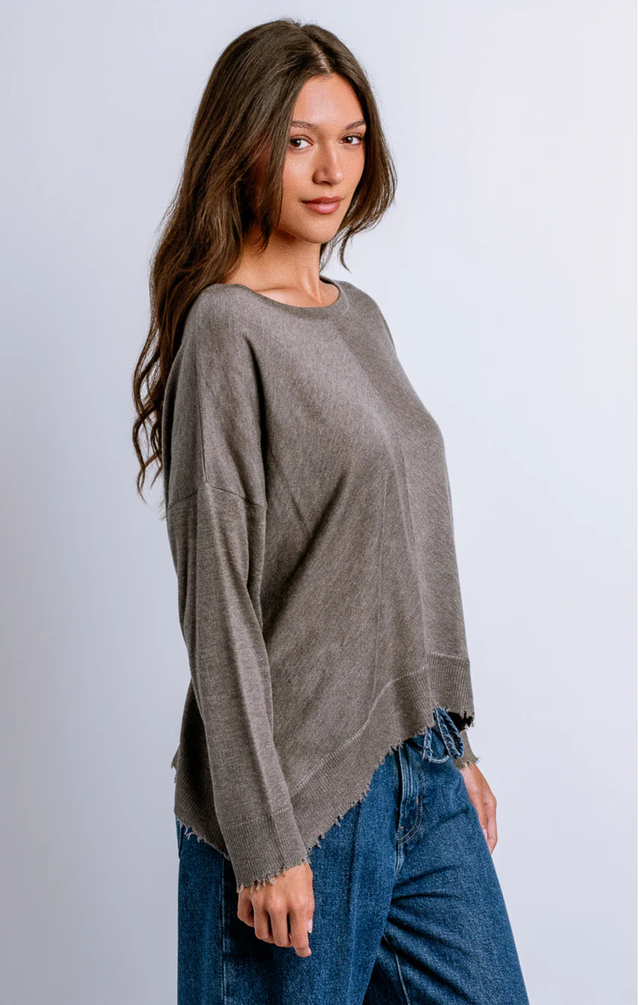 Woman wearing a gray sweater and blue jeans against a white background