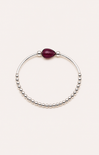 Bracelet with a red gemstone on a wrist against a beach sunset background