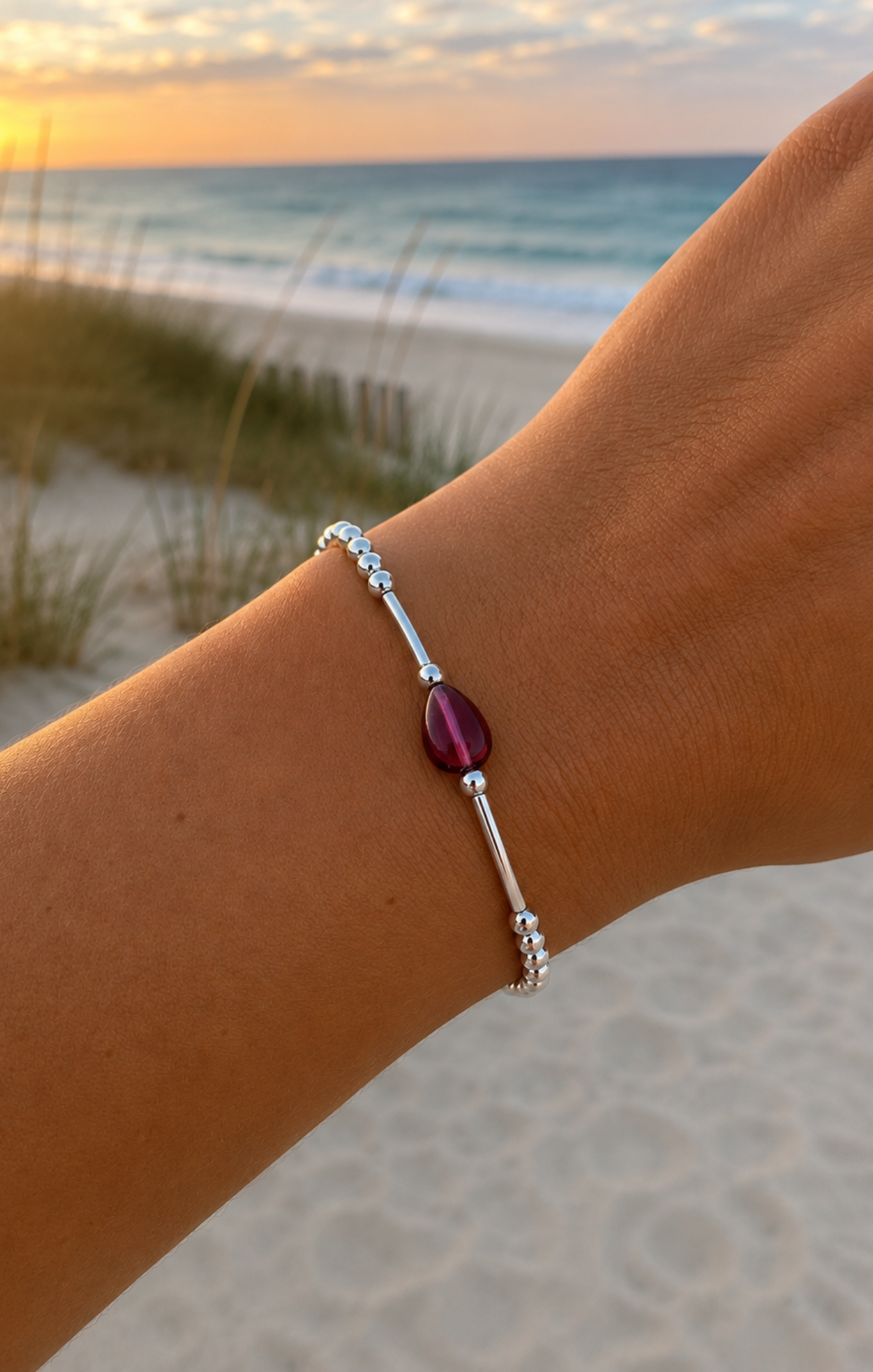 Bracelet with a red gemstone on a wrist against a beach sunset background