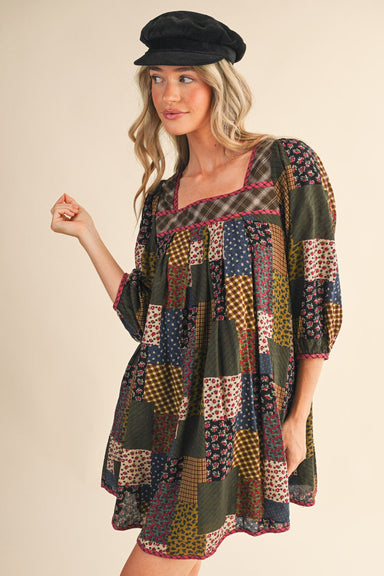 Woman wearing a patchwork dress and black cap against a beige background