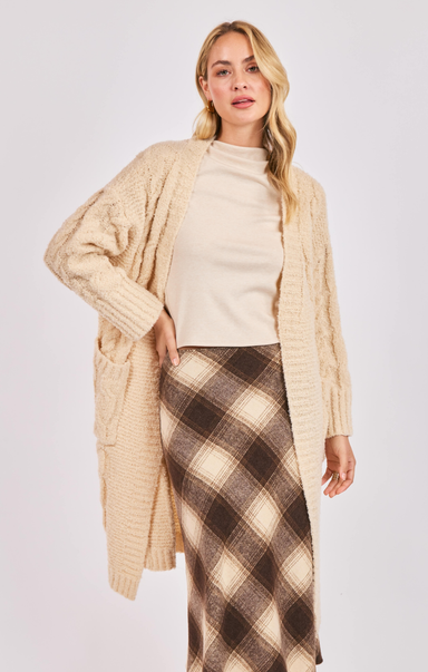 Woman wearing a beige cardigan and plaid skirt on a white background