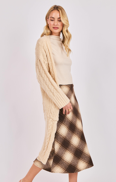 Woman wearing a cream cable knit sweater and plaid skirt on a white background