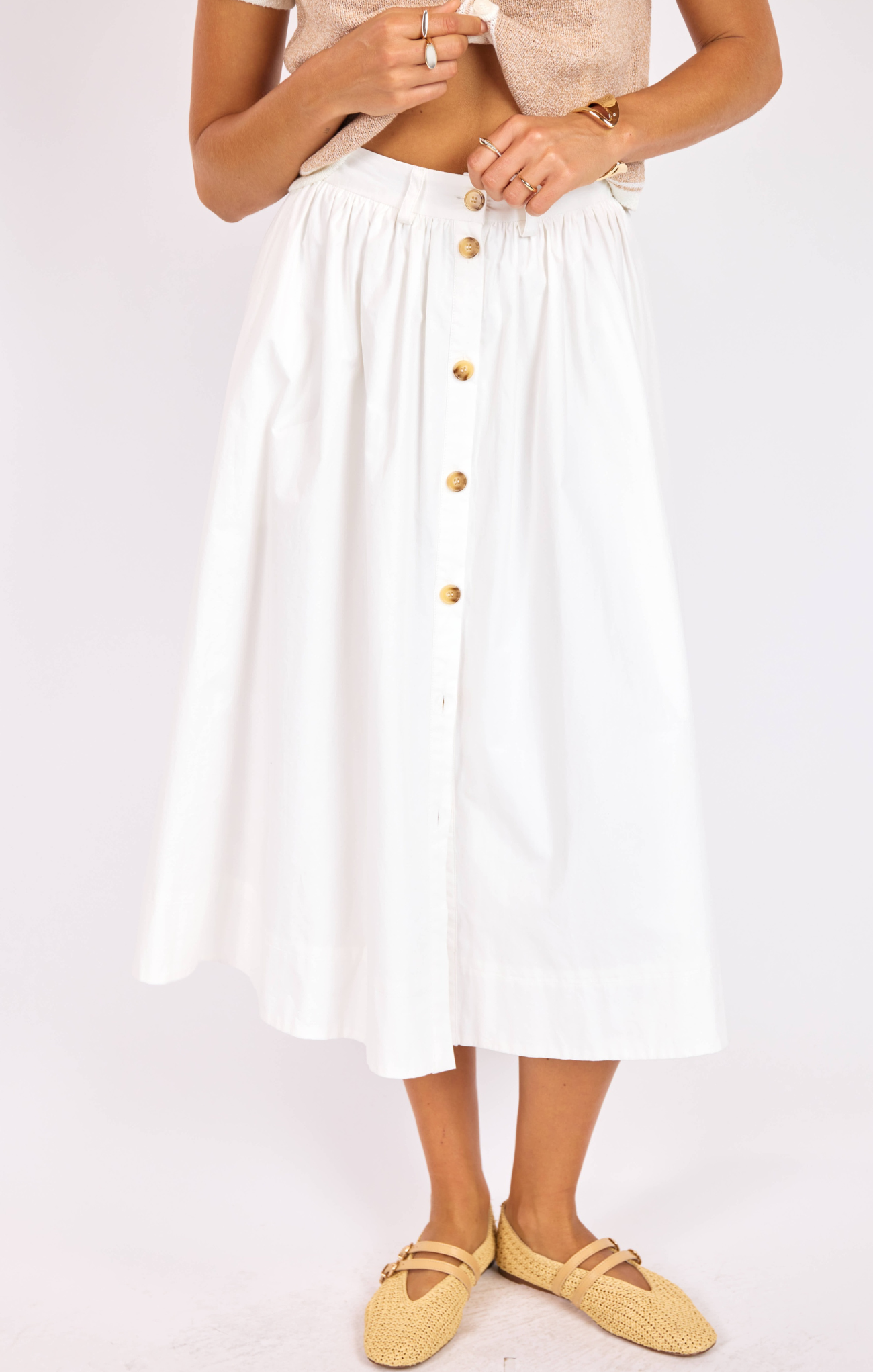Person wearing a white skirt with gold buttons on a plain background