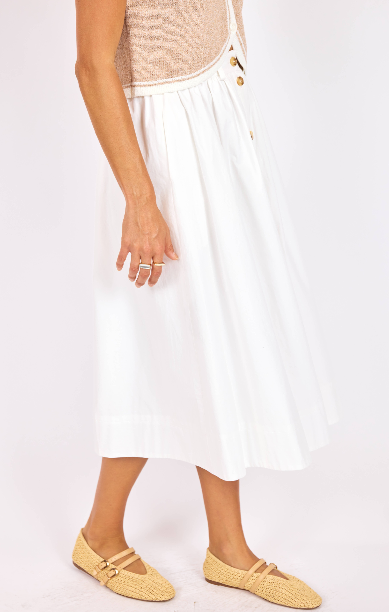 Person wearing a white skirt with gold buttons on a plain background