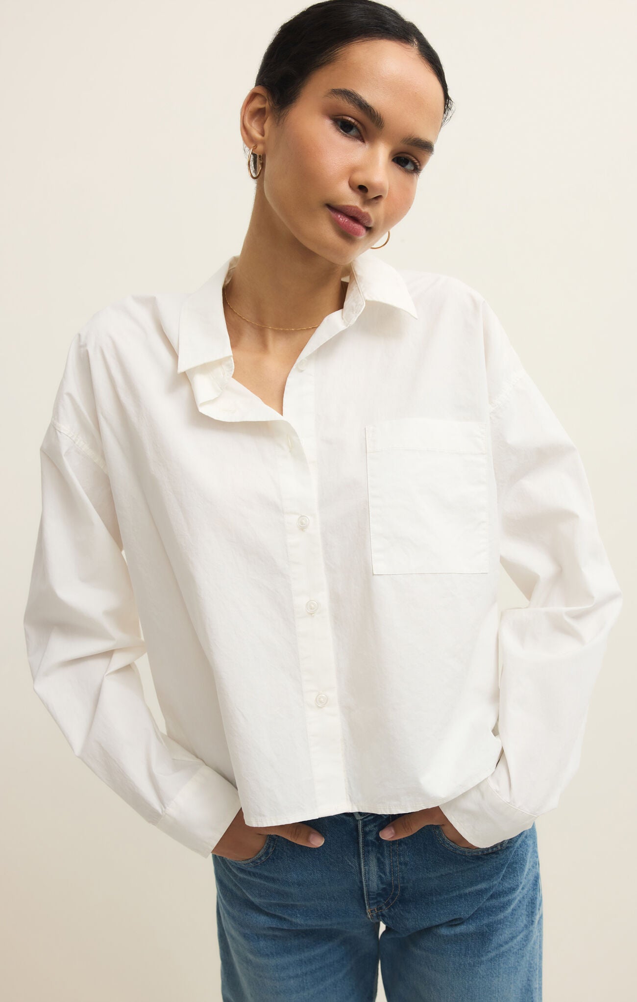 Woman wearing a white shirt and blue jeans against a plain background